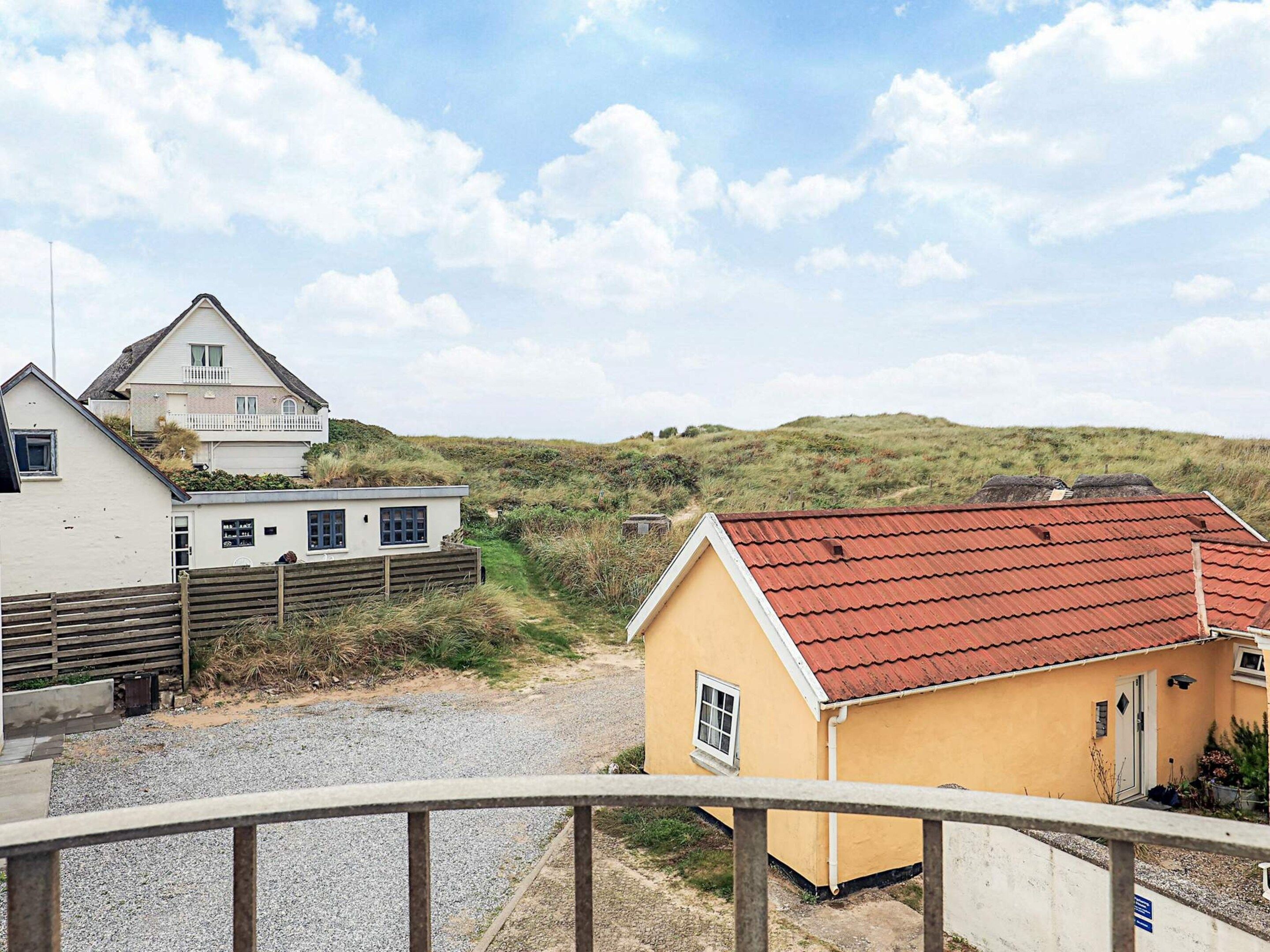A coastal property with a gravel driveway, a wooden fence, and a yellow building with a red roof.