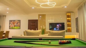 A billiards table in a room with a sofa, a television, and a decorative ceiling light fixture. - Smart 3-Bedroom Apartments – A Home Away From Home (Lagos)