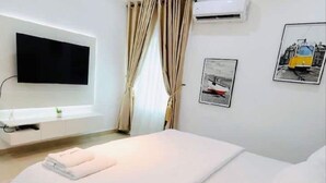 A hotel room with a bed, a flat-screen TV mounted on the wall, and two framed pictures on the wall. - Smart 3-Bedroom Apartments – A Home Away From Home (Lagos)