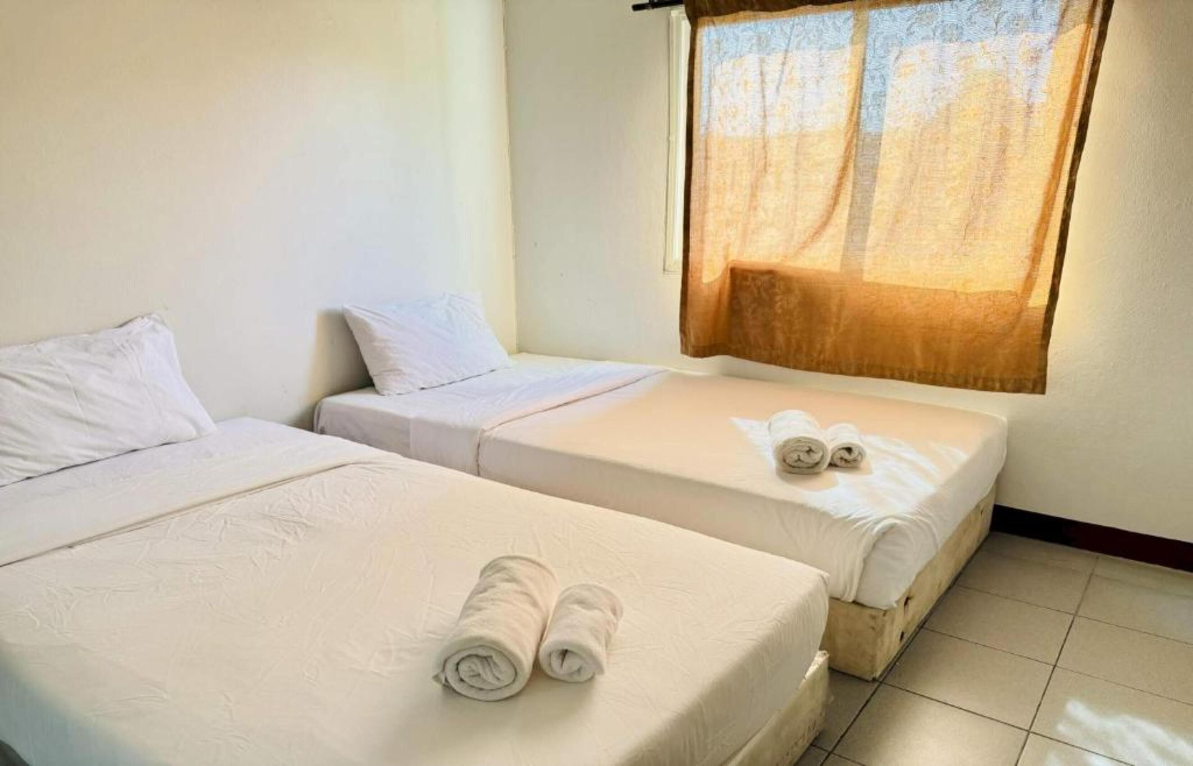 A hotel room with two beds, a window with a curtain, and rolled towels on the beds.