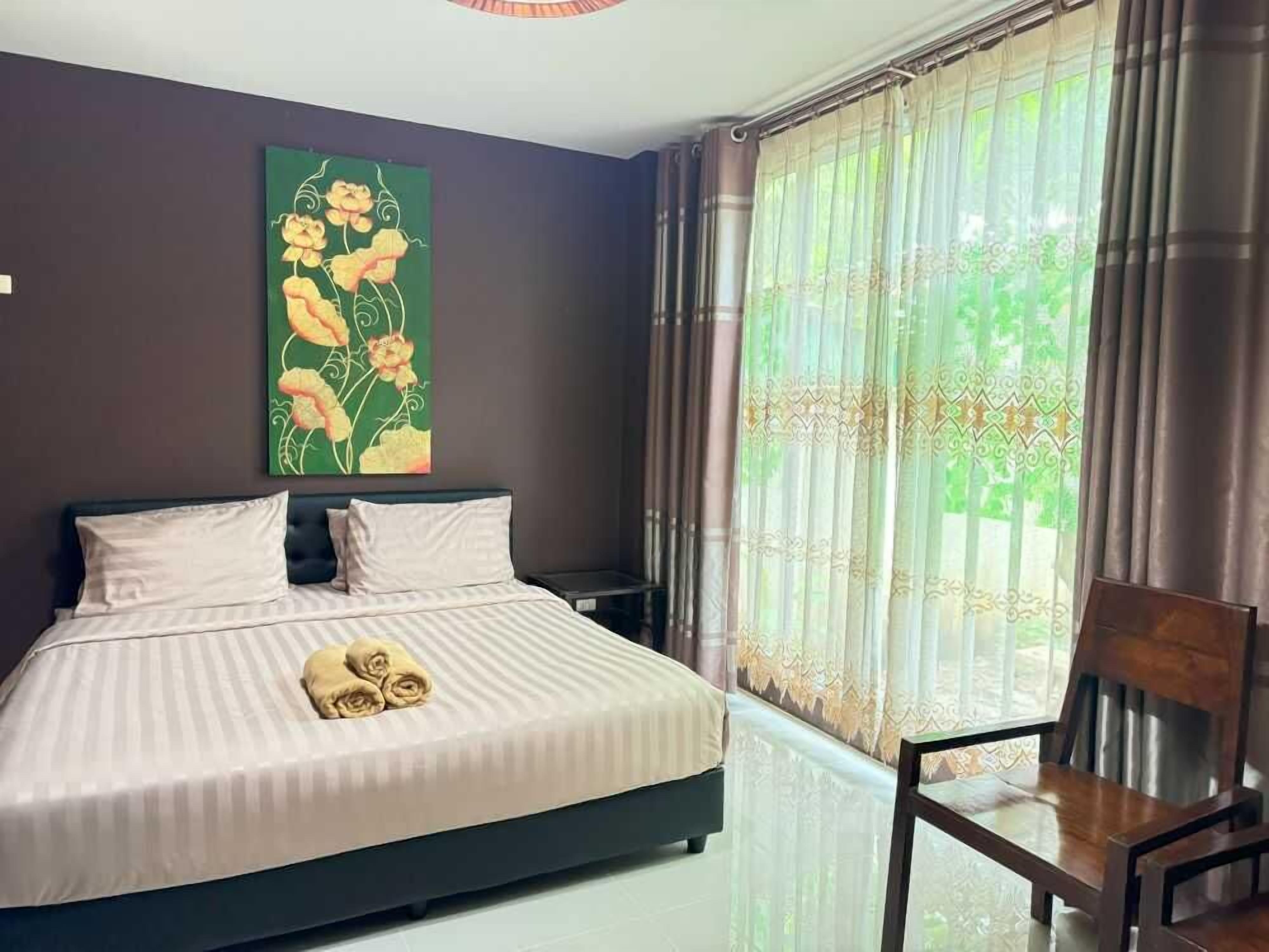 A bedroom with a bed, a chair, a painting on the wall, and a window with curtains.