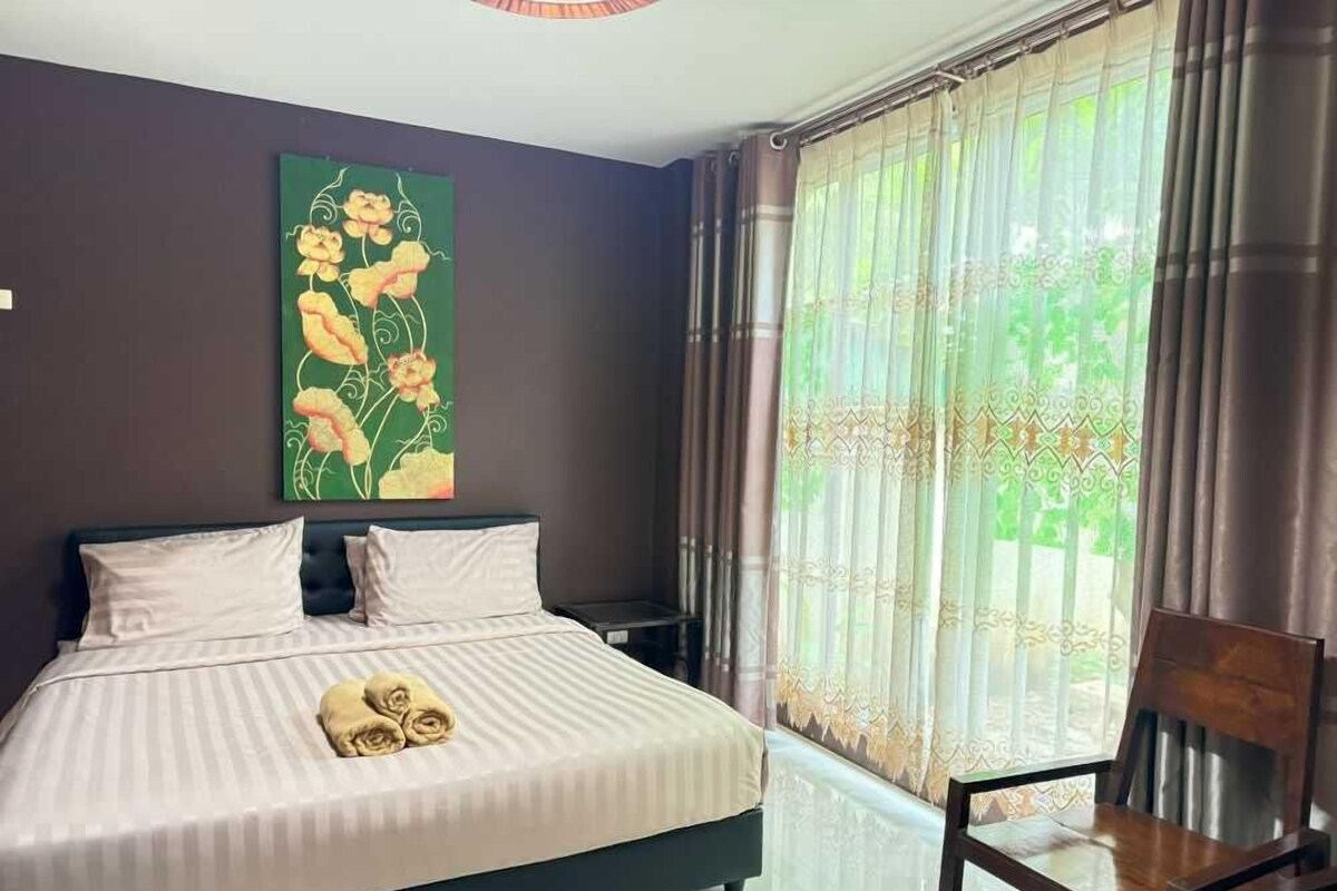 Une chambre à coucher avec un lit, une chaise, un tableau au mur et une fenêtre avec des rideaux.