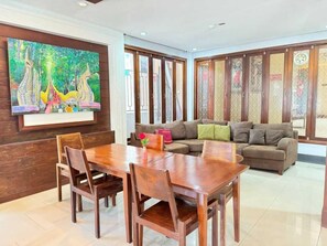 Un coin repas avec une table et des chaises en bois, un canapé avec des coussins et un grand tableau accroché au mur.