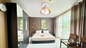 Ein Hotelzimmer mit einem großen Bett, einem Schreibtisch und einem Stuhl. An der Wand hängt eine Uhr und es gibt eine Deckenleuchte.