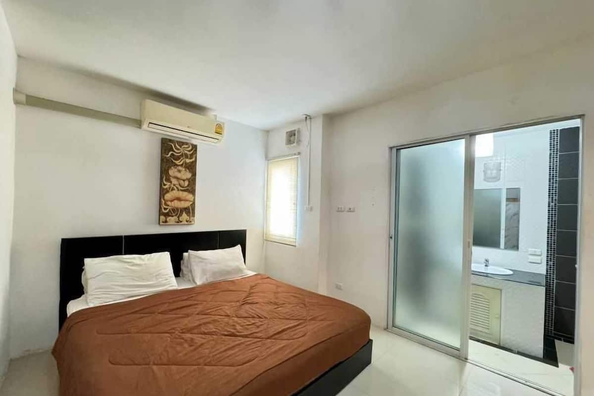 Un dormitorio con cama, aire acondicionado de pared, ventana y puerta corrediza de vidrio que da a un balcón.