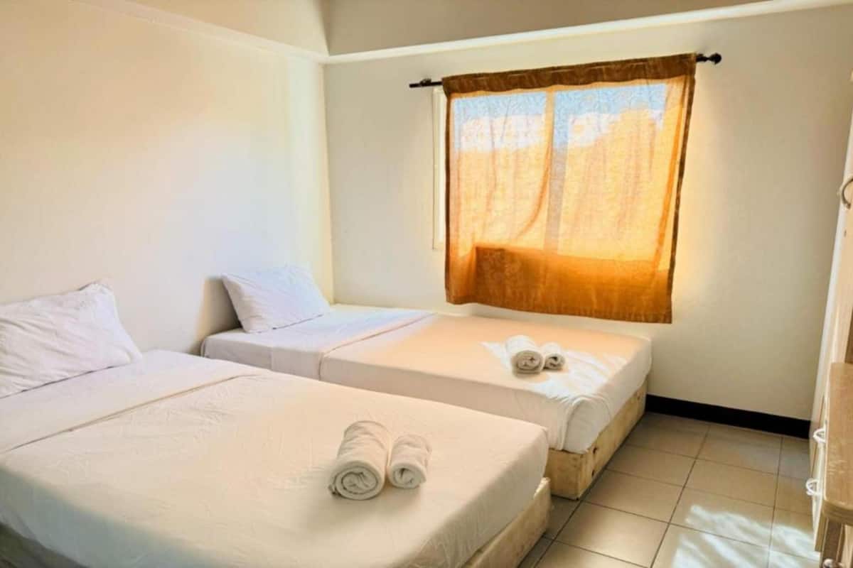 Una habitación de hotel con dos camas, una ventana con cortina y una silla de madera.