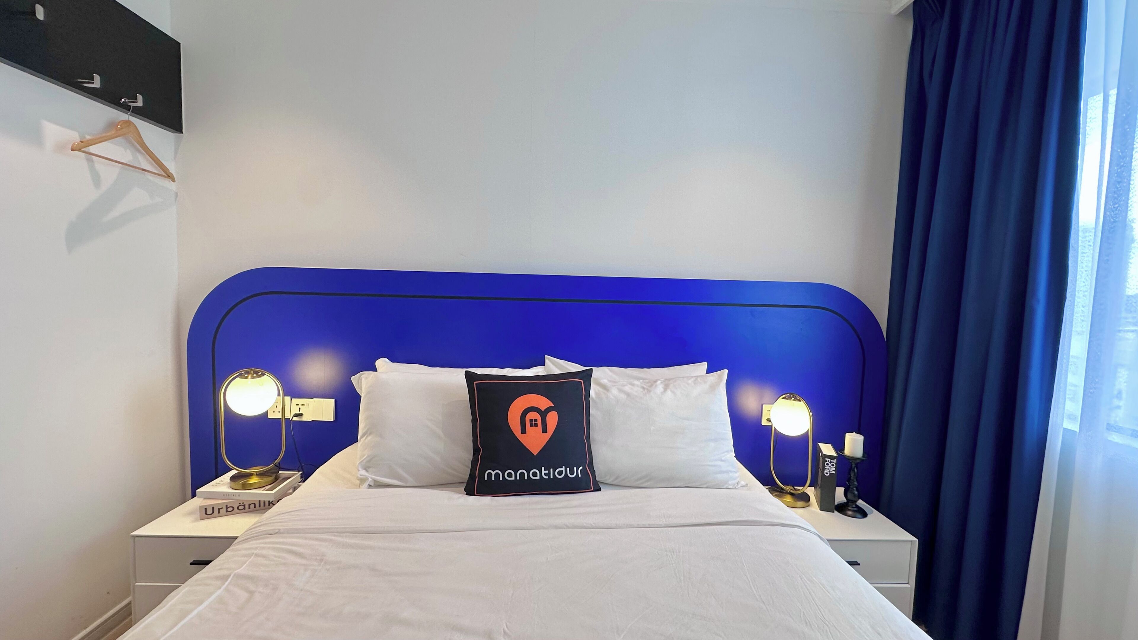 Een hotelkamer met een blauw hoofdeinde, witte beddengoed en een kussen met een hart en een huissymbool.