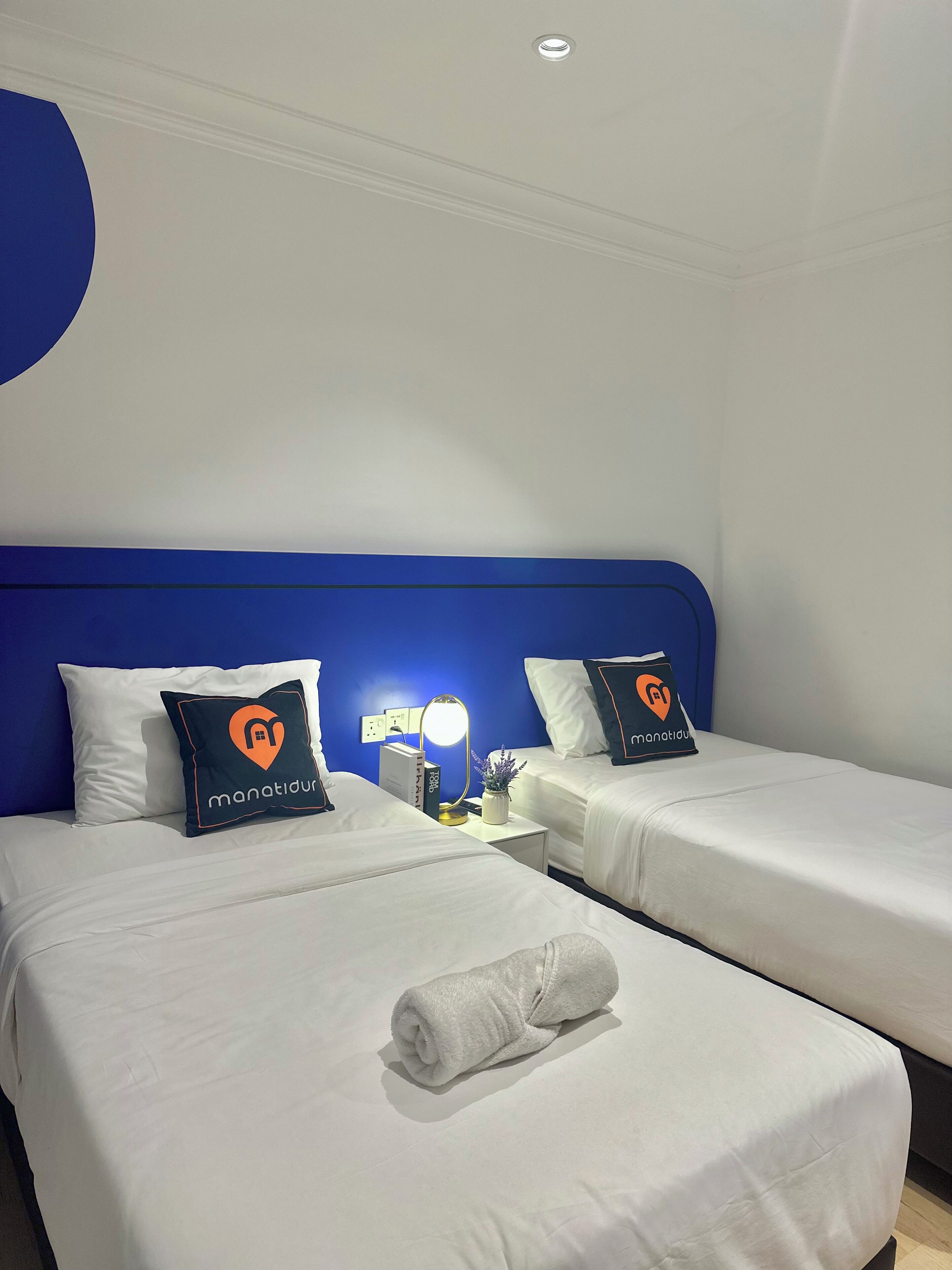 Habitación de hotel con dos camas individuales, una mesita de noche con lámpara y un enchufe.