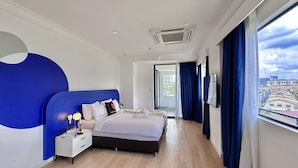 Quarto de hotel moderno com uma cama grande, mesa de cabeceira, televisão e vista para a cidade.
