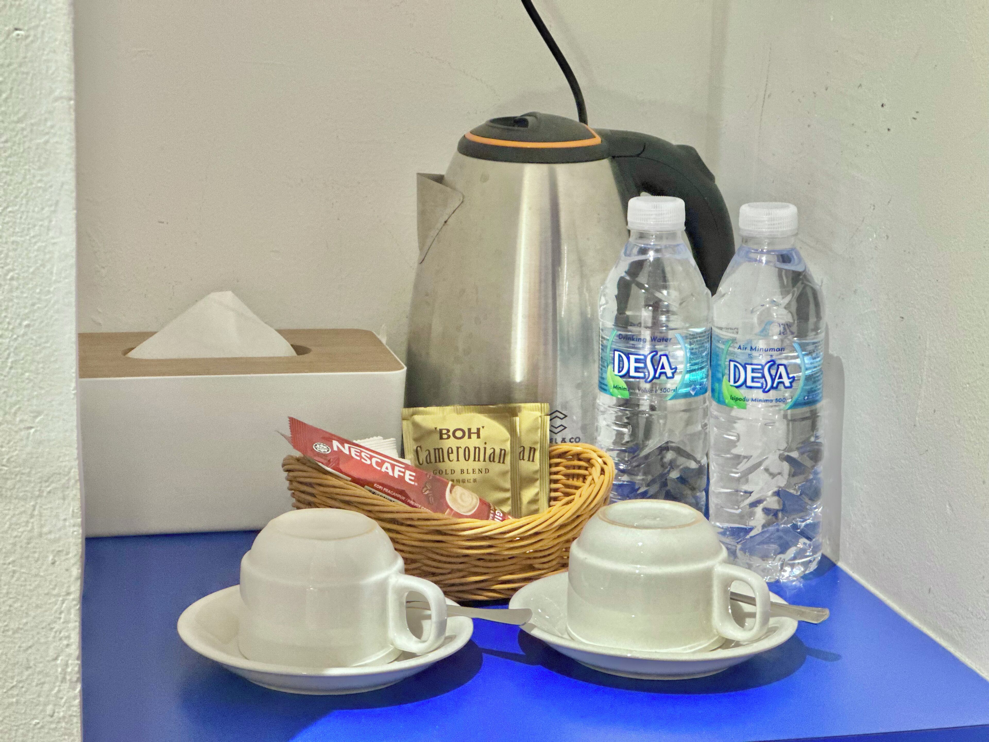 A kitchenette with a coffee maker, two water bottles, a basket with coffee pods, and two cups on a blue table.