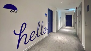 Corredor com um letreiro escrito 'hello', portas numeradas 605 e uma porta azul.