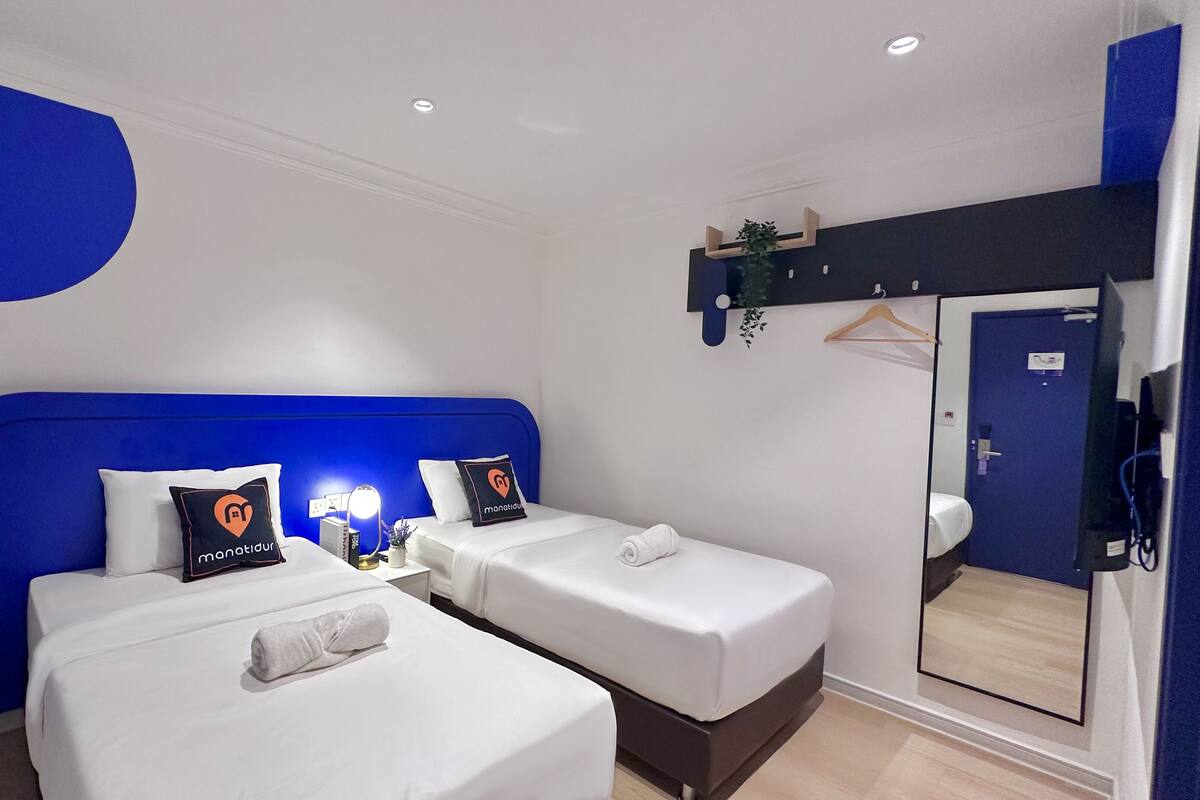 Ein Hotelzimmer mit zwei Betten, einem blauen Kopfteil, einem Nachttisch mit Lampe und einer blauen Tür.