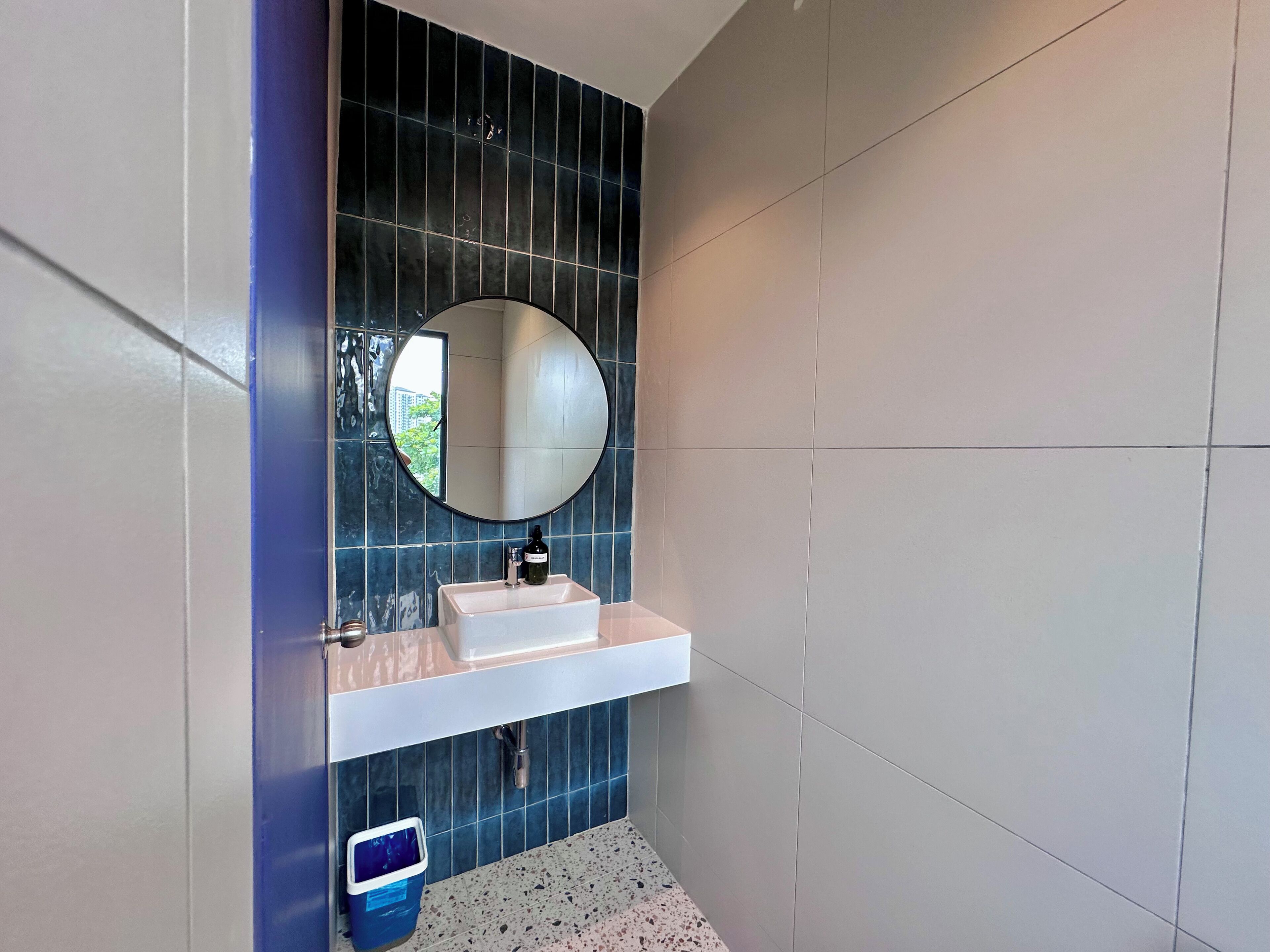 A bathroom with a white sink, a round mirror, and blue tiles on the wall.