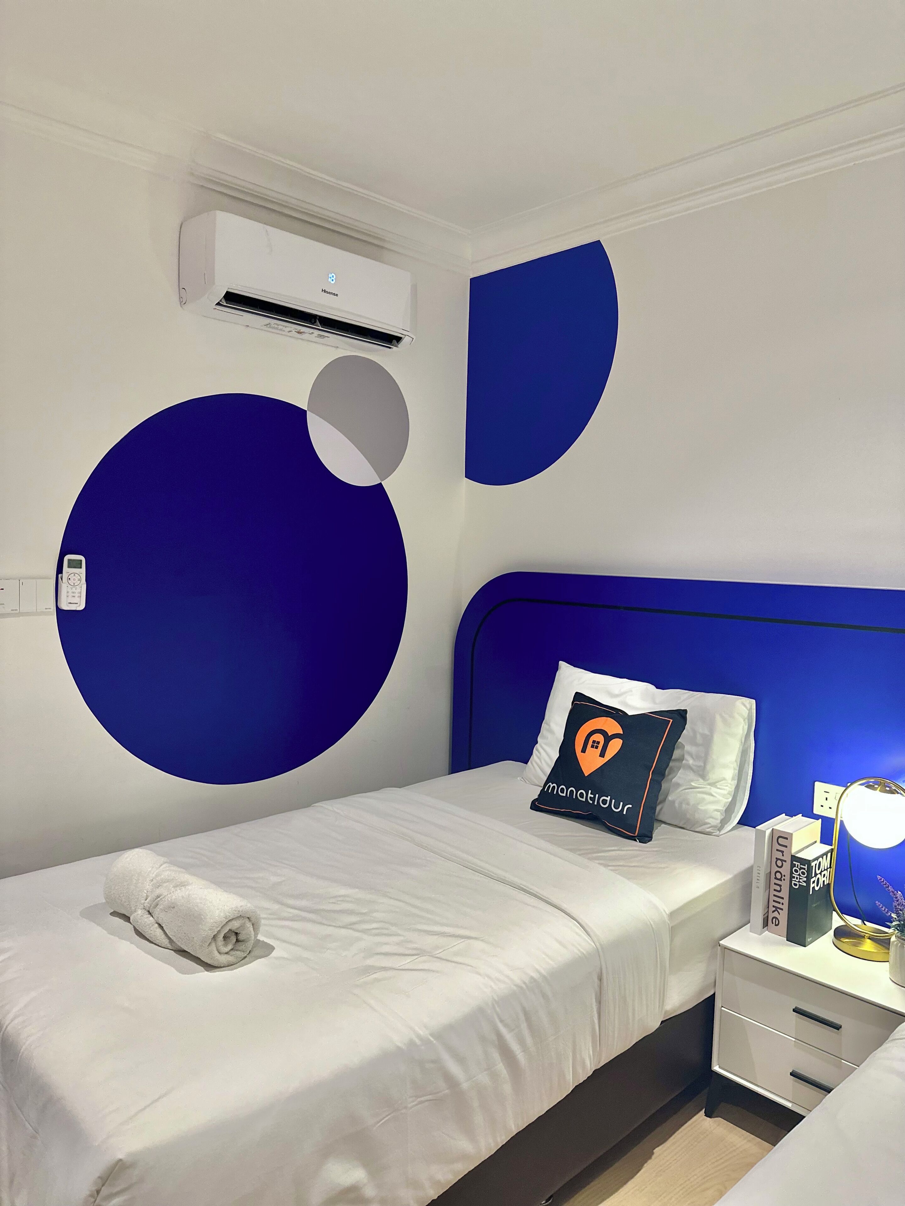 A hotel room with a bed, a nightstand, a lamp, and a wall-mounted air conditioner.