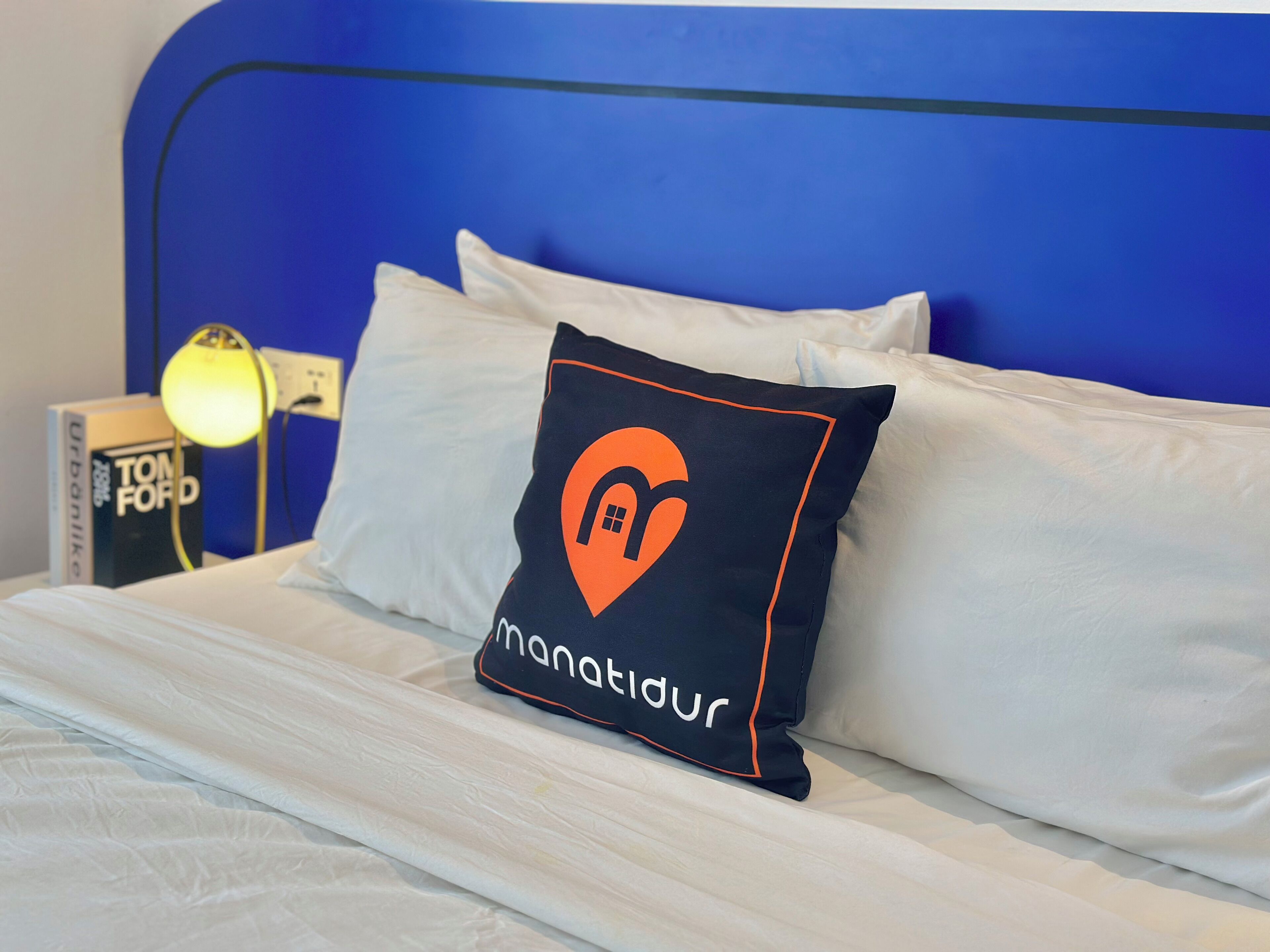 A bed with white linens, a blue headboard, and a pillow with a logo.