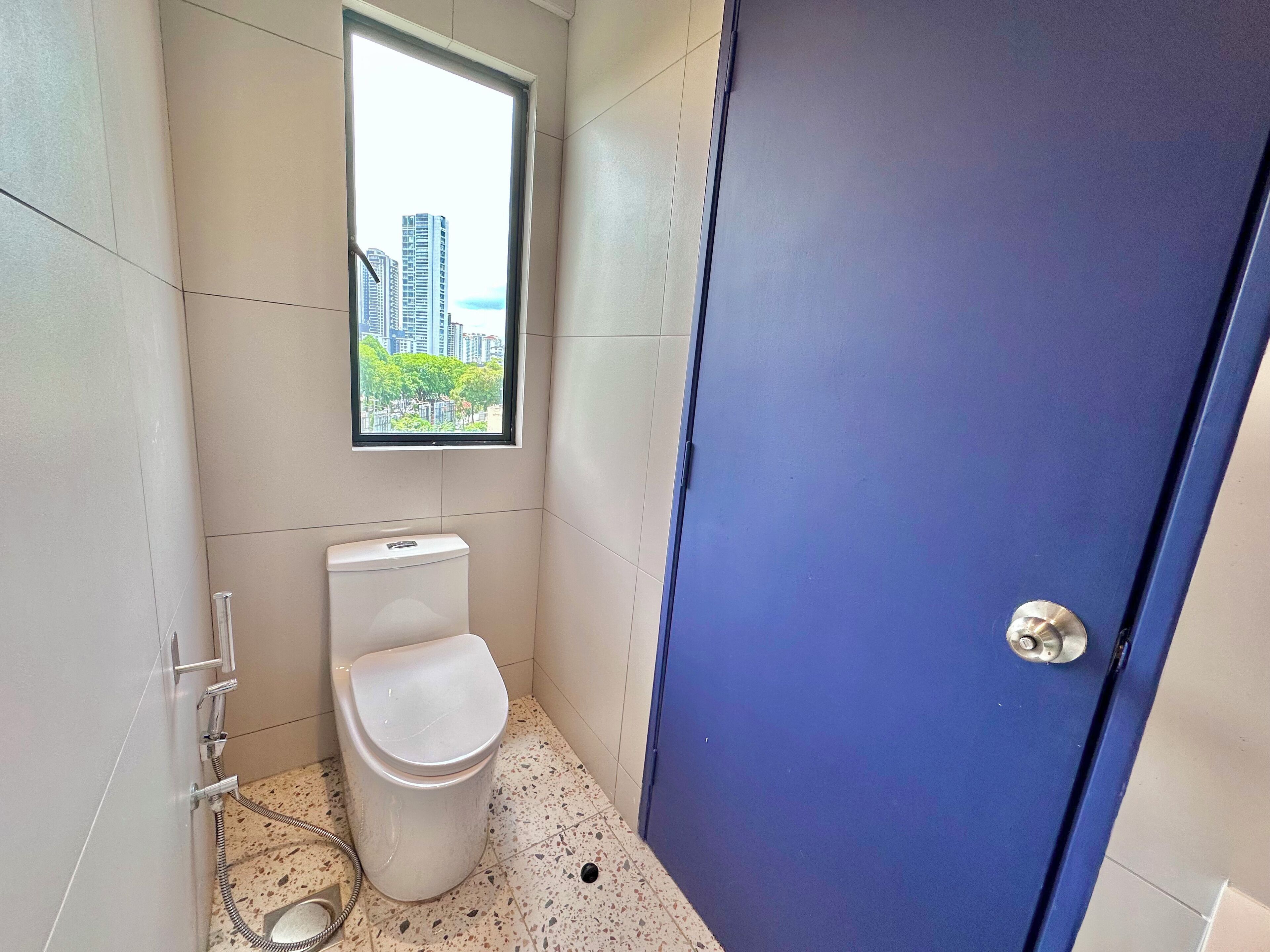 Ein kleines, modernes Badezimmer mit Toilette, Fenster und einer blauen Tür.