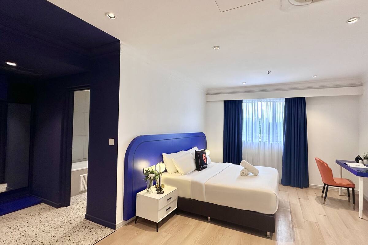 Ein modernes Hotelzimmer mit einem großen Bett, einem Nachttisch und einem Schreibtisch mit Stuhl.