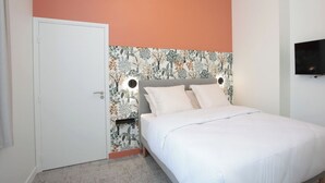 Quarto com cama, porta e televisão fixada na parede.