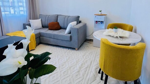 Una sala de estar moderna con un sofá gris, sillas amarillas, una mesita redonda y una planta en maceta.