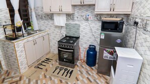 Una cocina con armarios de colores claros, estufa a gas, microondas y refrigerador.