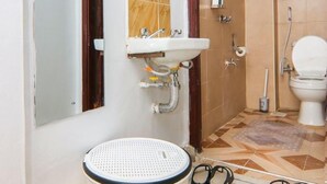 Un baño con lavamanos, espejo e inodoro. Hay dos cestas y un par de zapatos en el suelo.