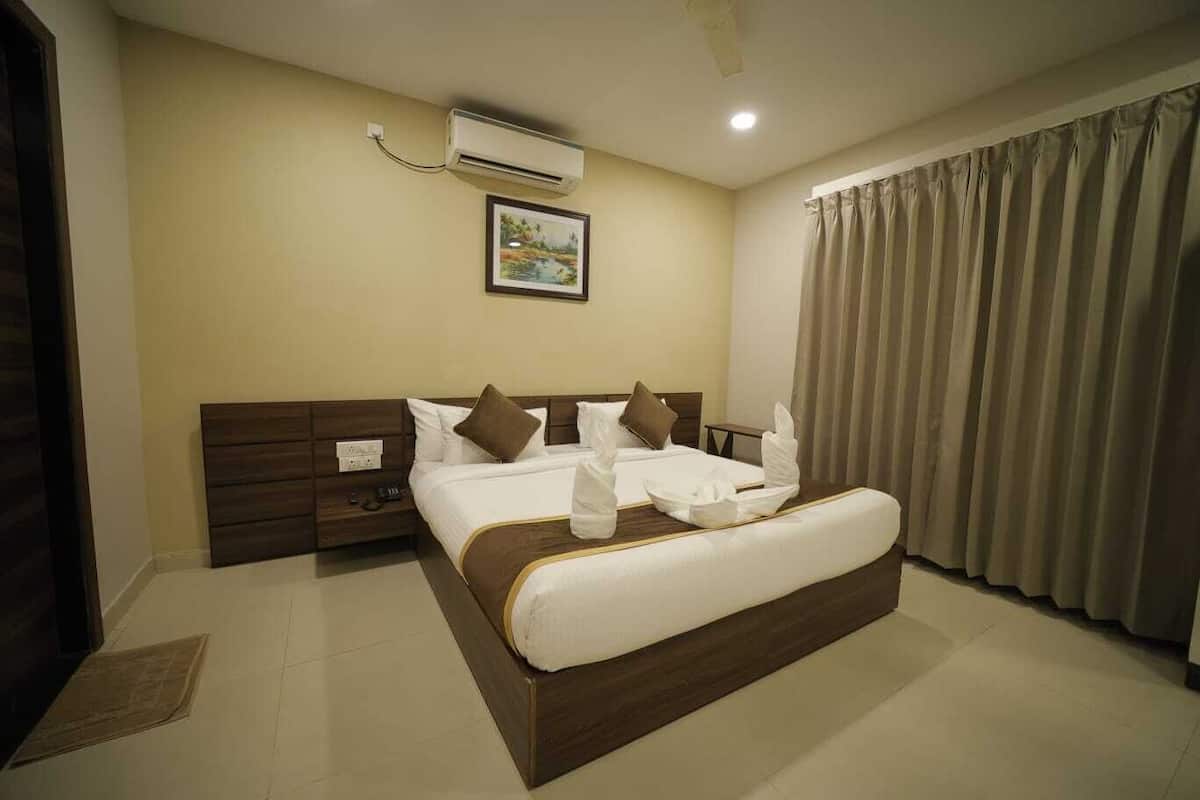 A hotel room with a large bed, a nightstand, a wall-mounted air conditioner, and a window with curtains.