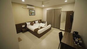 Une chambre d’hôtel comprenant un lit, des tables de chevet, un bureau, une chaise, un appareil de climatisation, un ventilateur de plafond et un grand miroir.