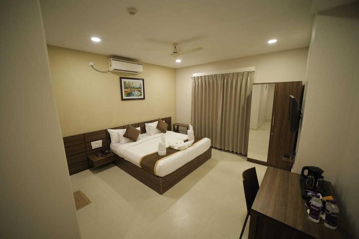 A hotel room with a bed, bedside tables, a desk, a chair, an air conditioning unit, a ceiling fan, and a large mirror.