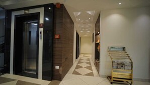 Un hall d’hôtel au design moderne, avec un sol à motifs à carreaux, un ascenseur fixé au mur et un kiosque à journaux proposant des magazines.