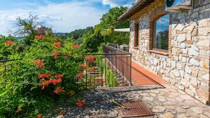 A stone building with a balcony overlooking a garden with red flowers.