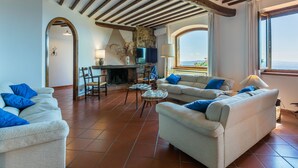 A spacious living room with a fireplace, comfortable seating, and a view of the sea.