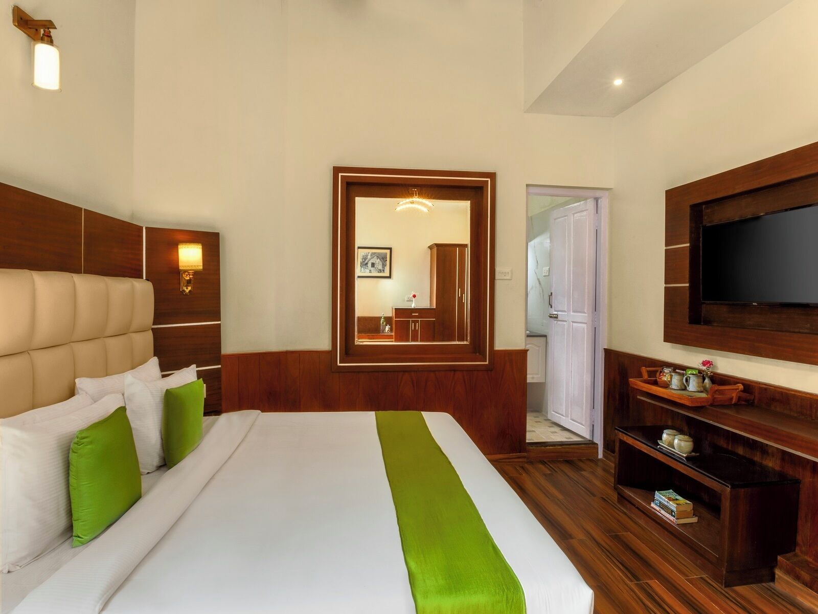 Ein Hotelzimmer mit einem großen Bett, einem Holz-Kopfteil, einem Flachbildfernseher, einem Holzschreibtisch und einem Spiegel.