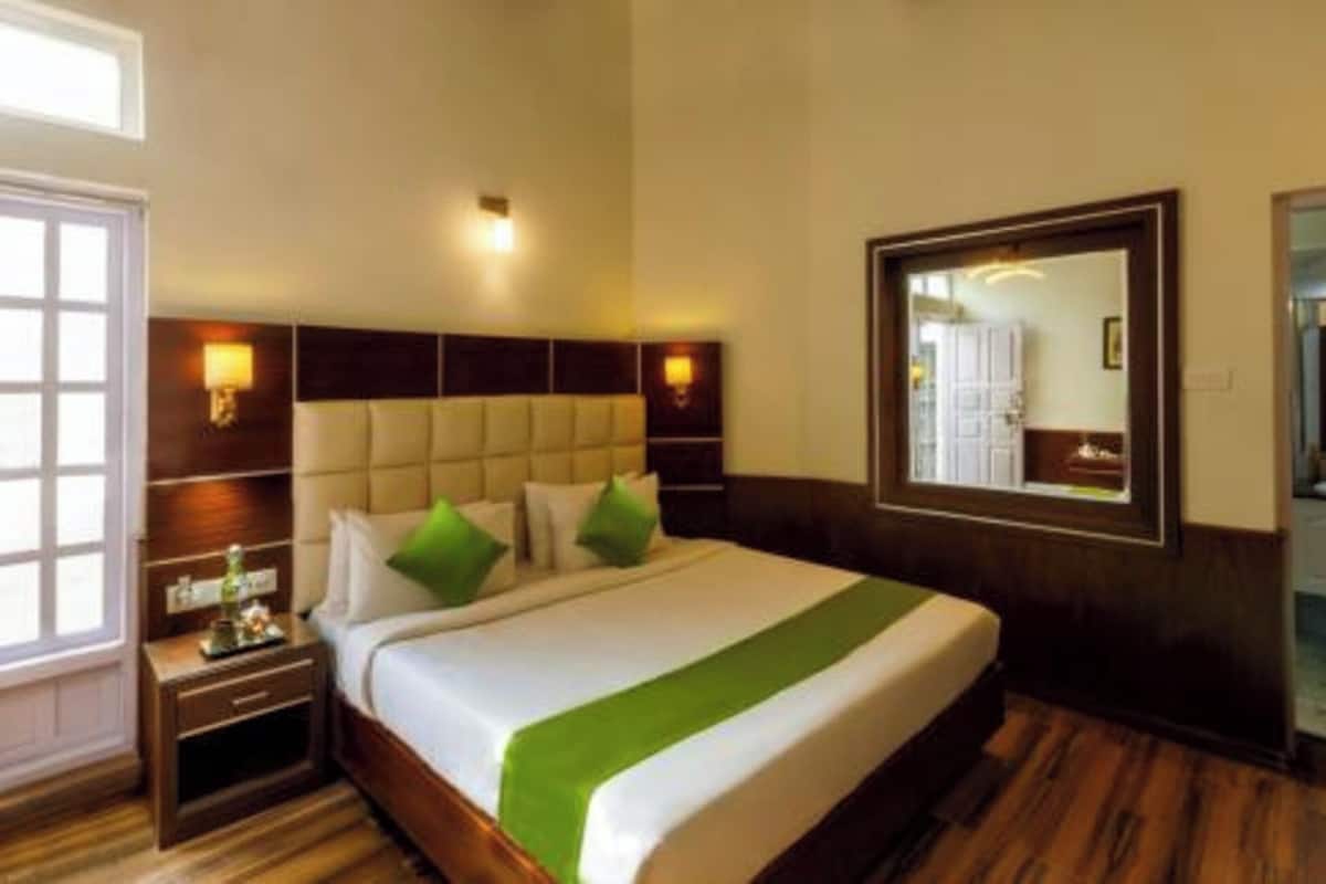 Una habitación de hotel con una cama grande, una mesita de noche, un espejo y una ventana.