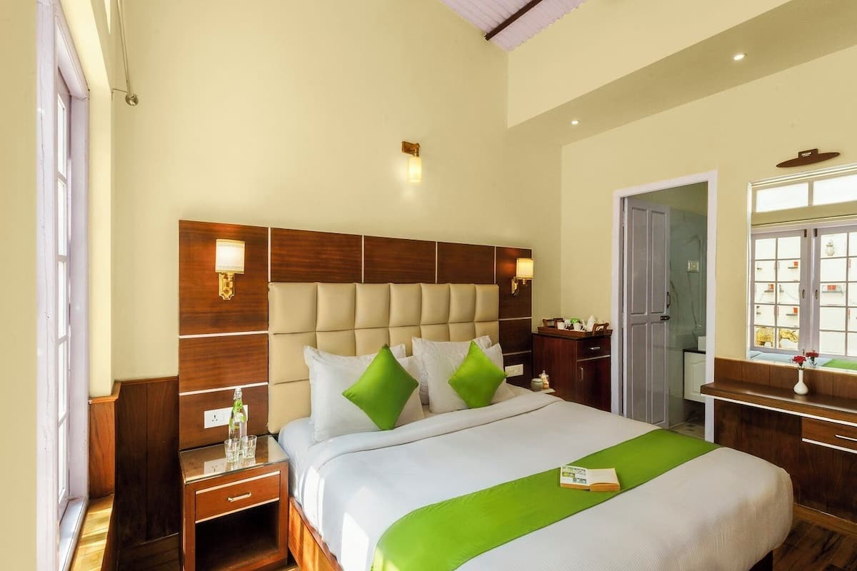 Habitación de hotel con una cama grande, cabecero de madera, mesitas de noche, cómoda y una ventana con vistas.