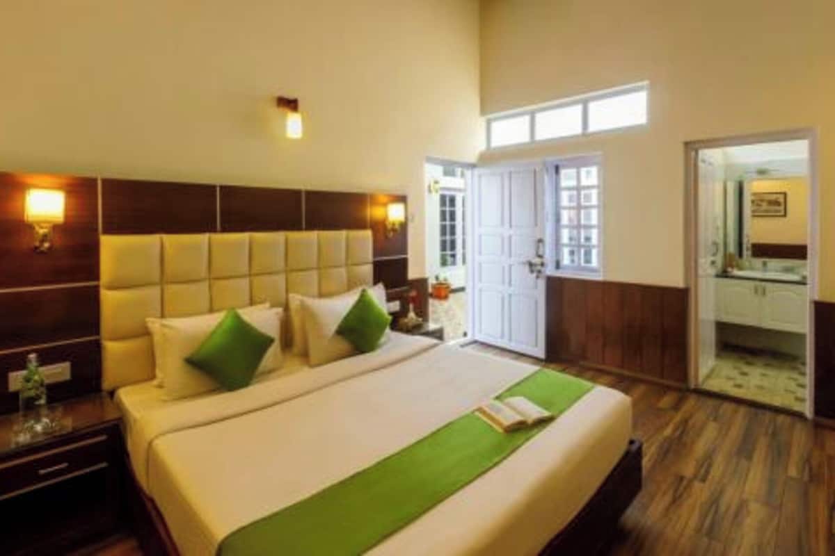 Habitación de hotel con una cama grande, cabecero de madera, lámparas de noche y vistas al exterior a través de una puerta.
