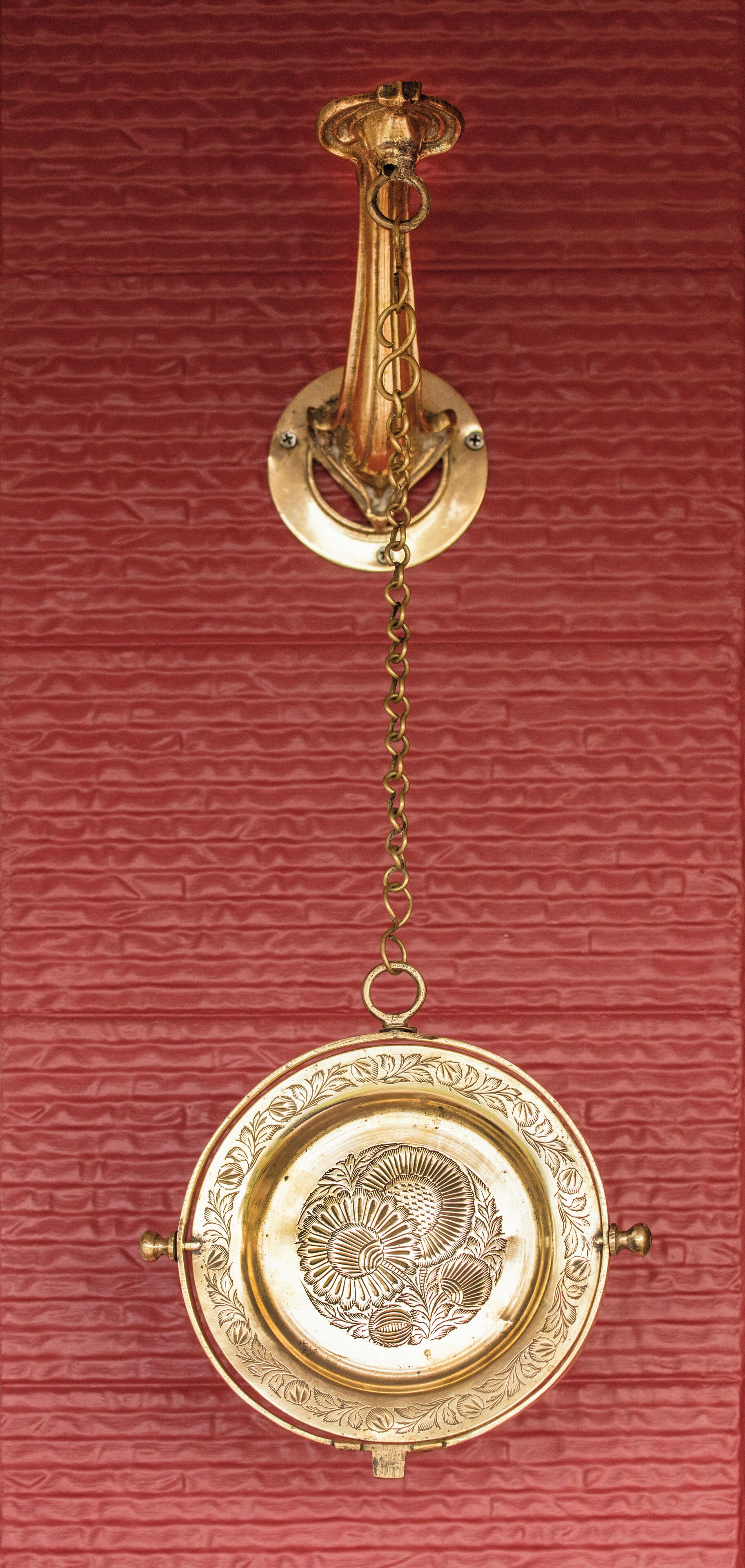 A brass door knocker with a floral design on a red textured wall.