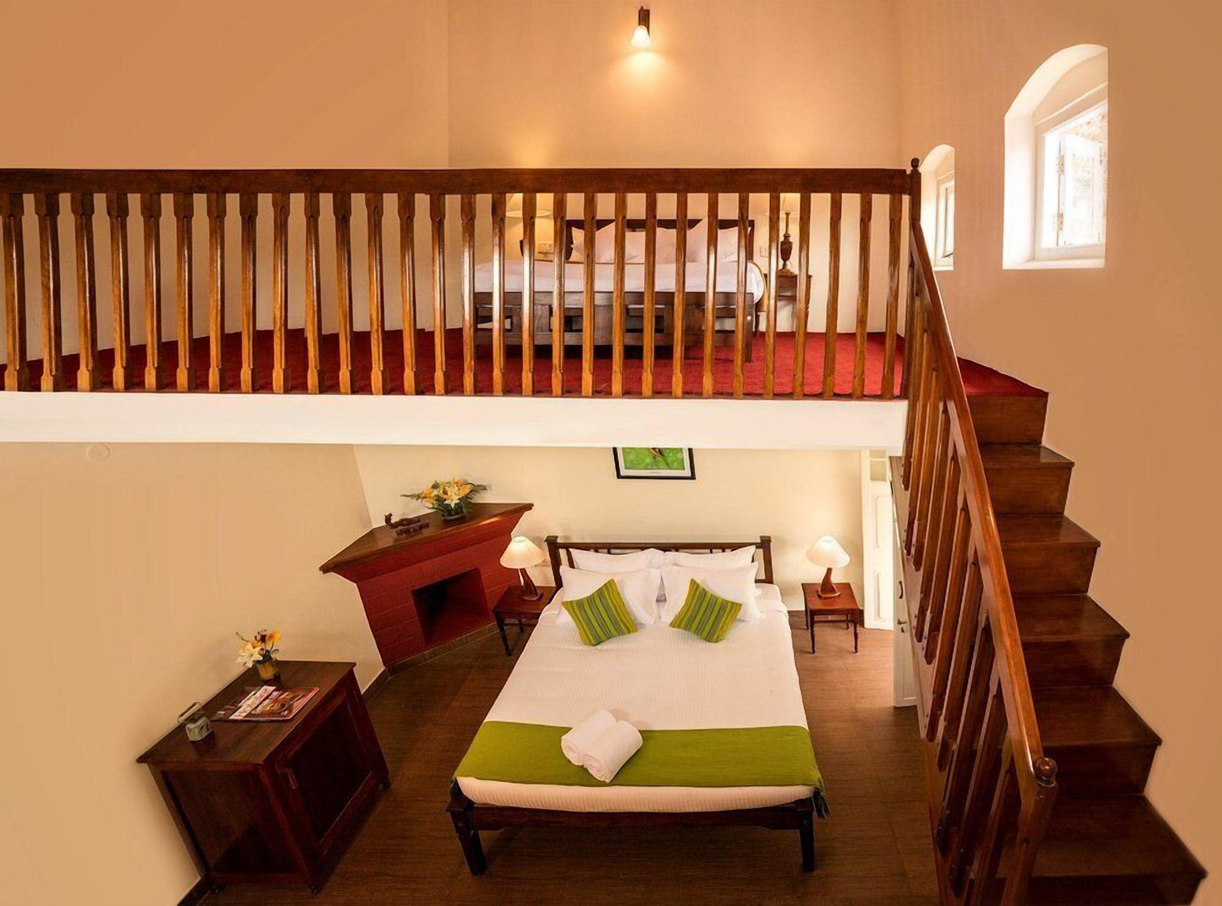 A hotel room with a bed, a desk, a small fireplace, a nightstand, and a staircase.