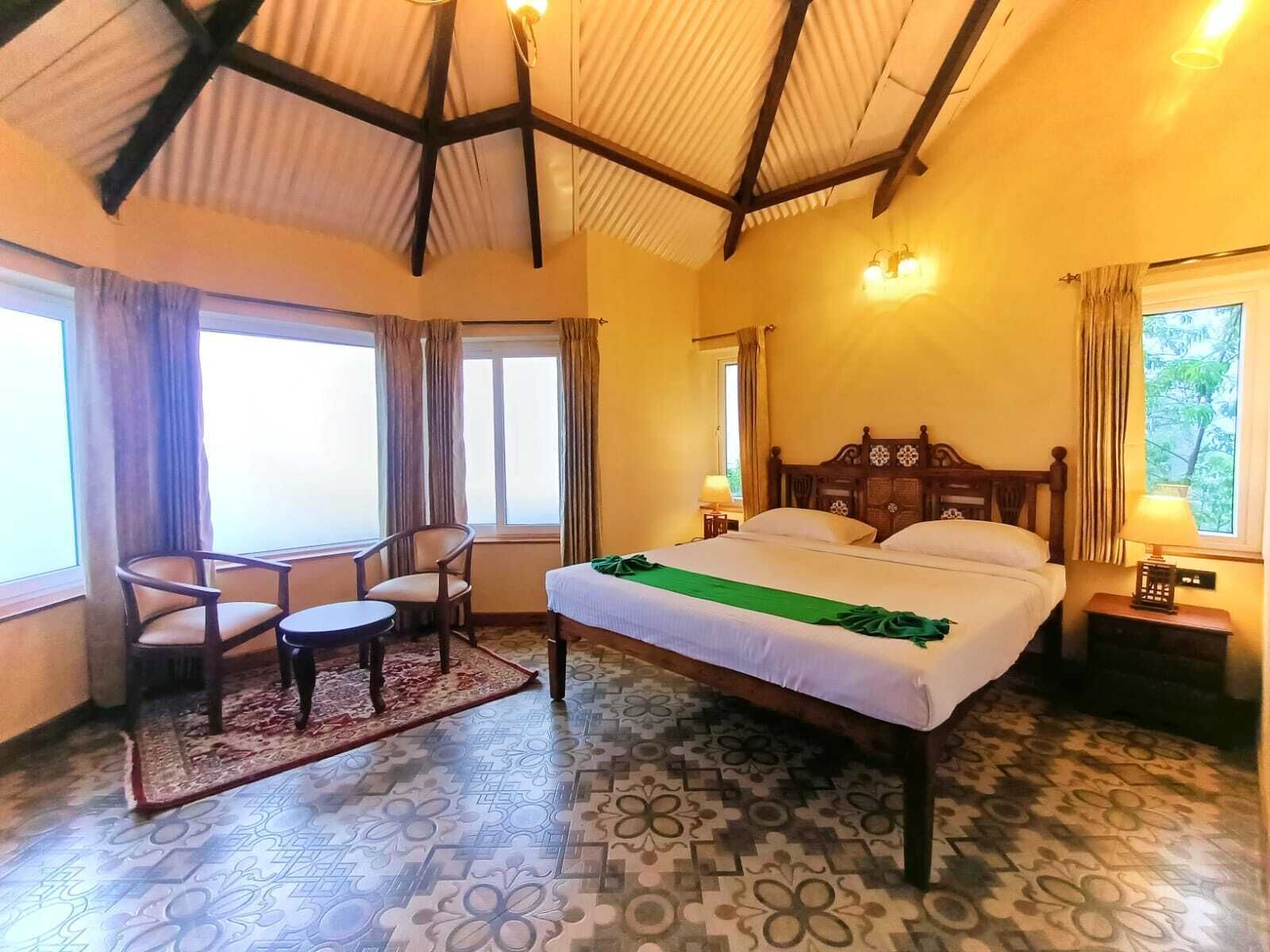 Habitación de hotel con una cama grande, dos sillones, una mesita y un ventanal con cortinas.