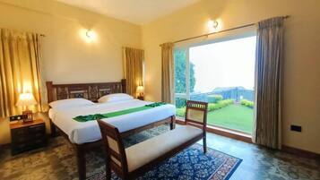 A hotel room with a bed, a bench, a nightstand, and a view of a garden through a large window.