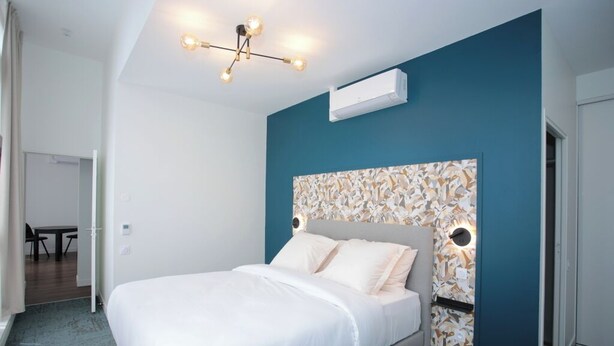 A modern hotel room with a large bed, a ceiling light fixture, and a wall-mounted air conditioner.