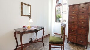 A room with a wooden desk, a mirror, a lamp, a chair, and a dresser.