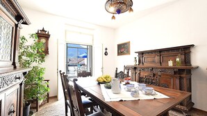 A dining area with a wooden table, chairs, and a chandelier. There is a window with a view of a mountain and a blue umbrella outside.