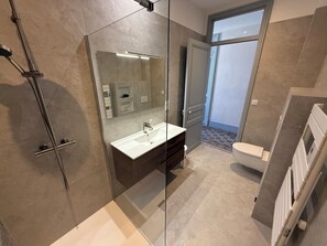 Uma casa de banho moderna com chuveiro de vidro, lavatório branco e sanita.