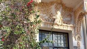 Une façade d’immeuble ornée d’un portail noir travaillé, un mur décoratif avec des sculptures florales et une enseigne indiquant un point d’information touristique.