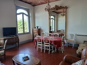 Uma sala de jantar com uma mesa redonda, cadeiras, uma televisão e um espelho grande.