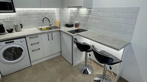 A modern kitchen with white cabinetry, a built-in washing machine, a sink, and two bar stools. - Central Studio next to Metro (Pireaus)