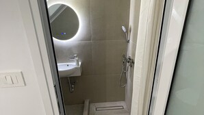 A modern bathroom with a glass shower enclosure, a sink, and a toilet. - Central Studio next to Metro (Pireaus)