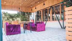 An outdoor seating area with purple chairs and a wooden table, surrounded by large windows and a tiled floor. - Sabah Hotel (Baku)