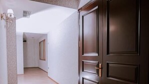 A hallway with wooden flooring, a dark wooden door, and a light-colored wall. - Sabah Hotel (Baku)