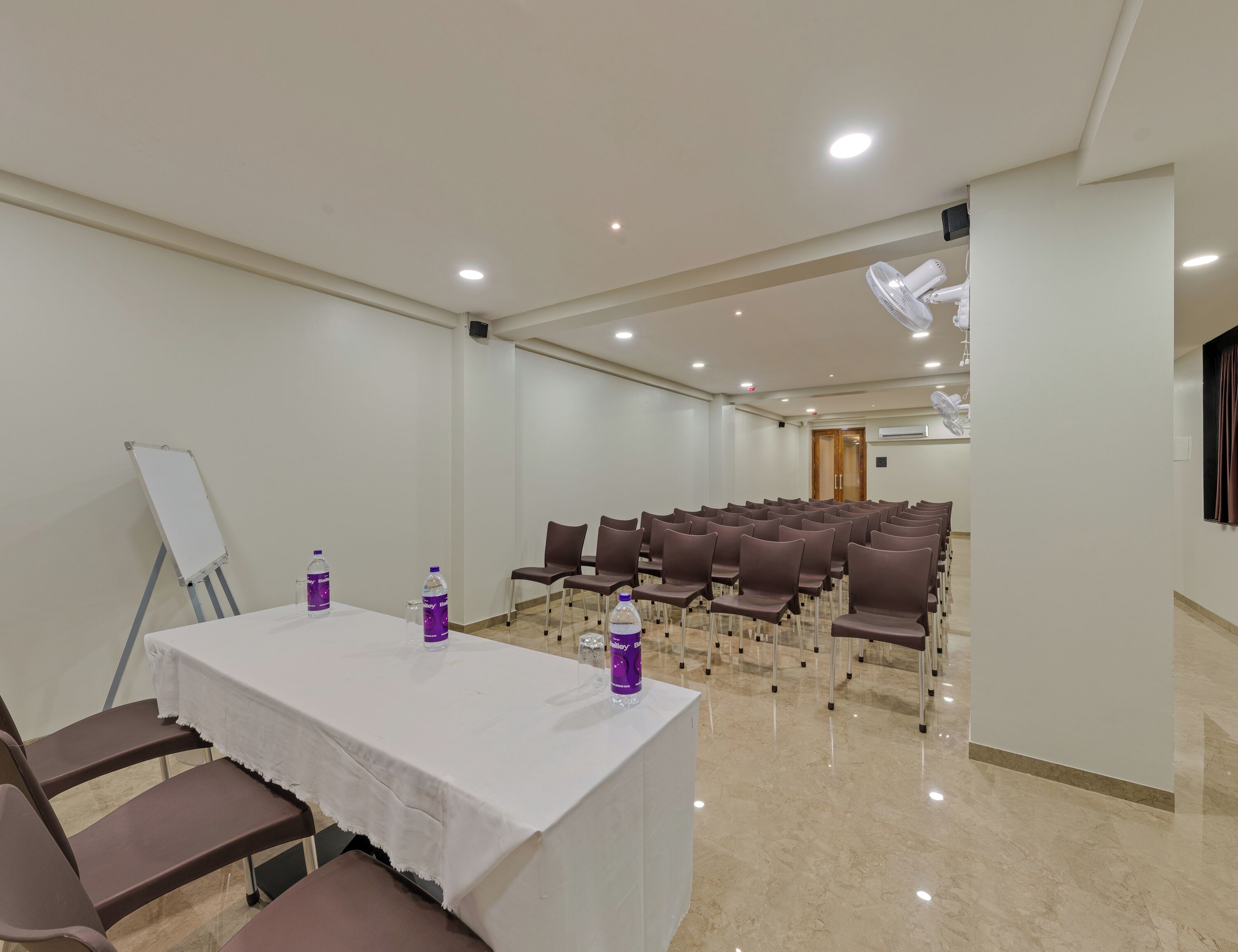 Un salón de conferencias con una mesa blanca, sillas marrones, una pizarra y botellas de agua.